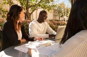 学生 sit outside at a table on a sunny day. 他们在笑.